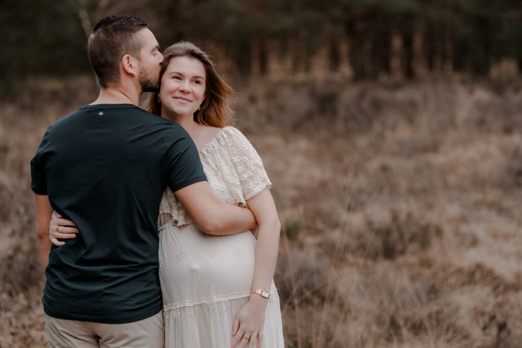 Een intiem moment tussen een zwangere vrouw en haar partner tijdens een zwangerschapsshoot in de omgeving van apeldoorn