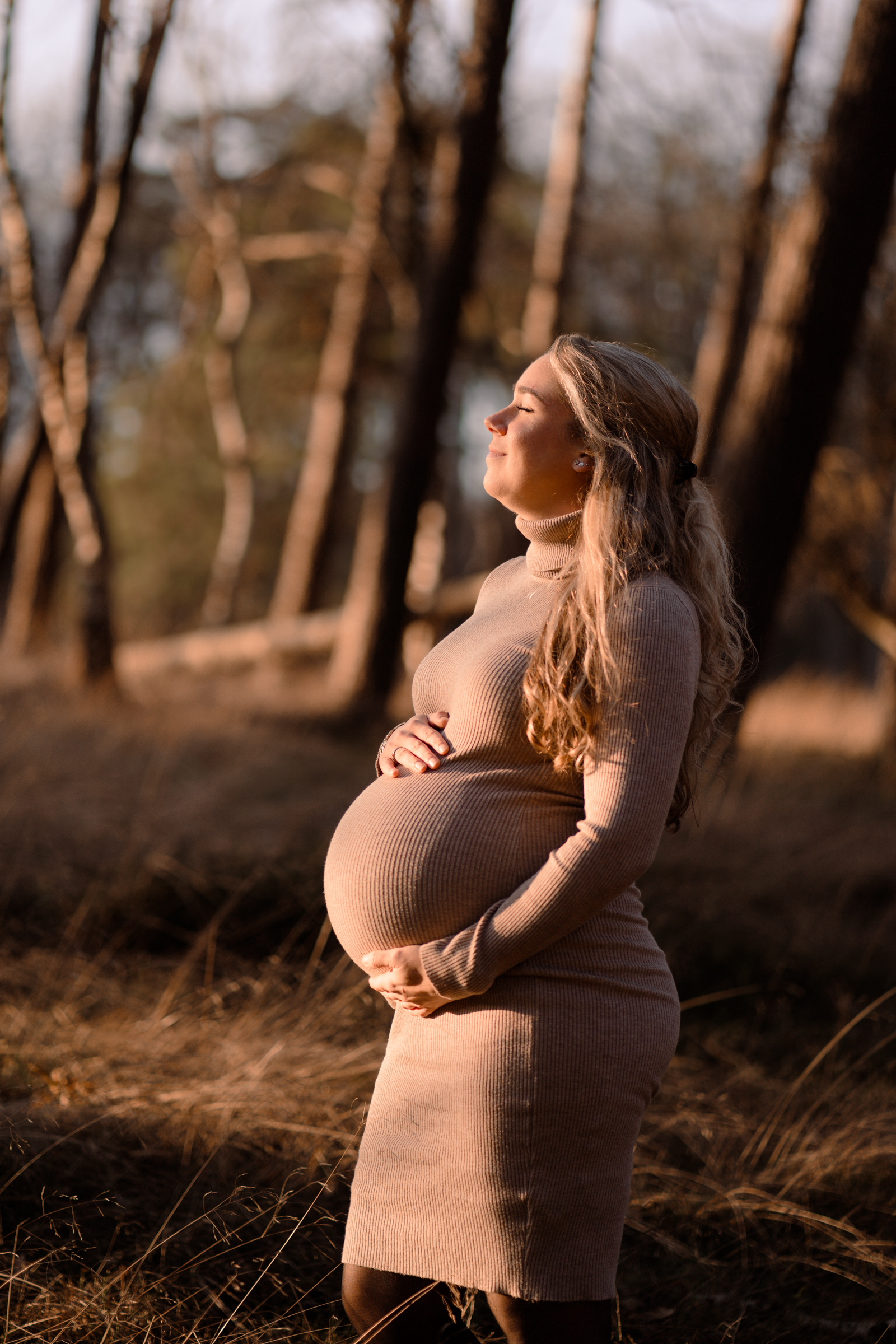 Zwangere vrouw in een warme, natuurlijke omgeving, genietend van de zonnestralen op haar gezicht tijdens een zwangerschapsshoot