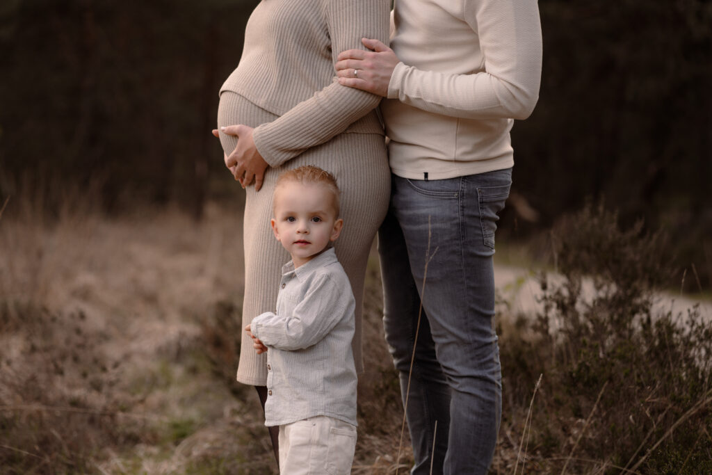 Zoontje staat voor papa en mama met haar zwangere buik in een spontaan moment gevangen tijdens een zwangerschapsshoot in de omgeving Apeldoorn