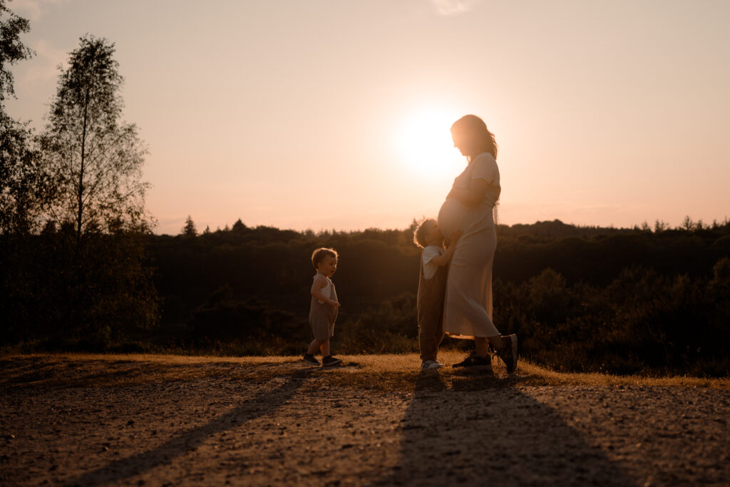 Zwangere moeder met haar twee zoontjes voor de ondergaande zon als half silhouetten tijdens een zwangerschapsshoot in Apeldoorn