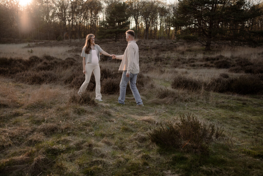 Zwangere vrouw wordt door partner door de heide geleid tijdens een zwangerschapsshoot in Apeldoorn