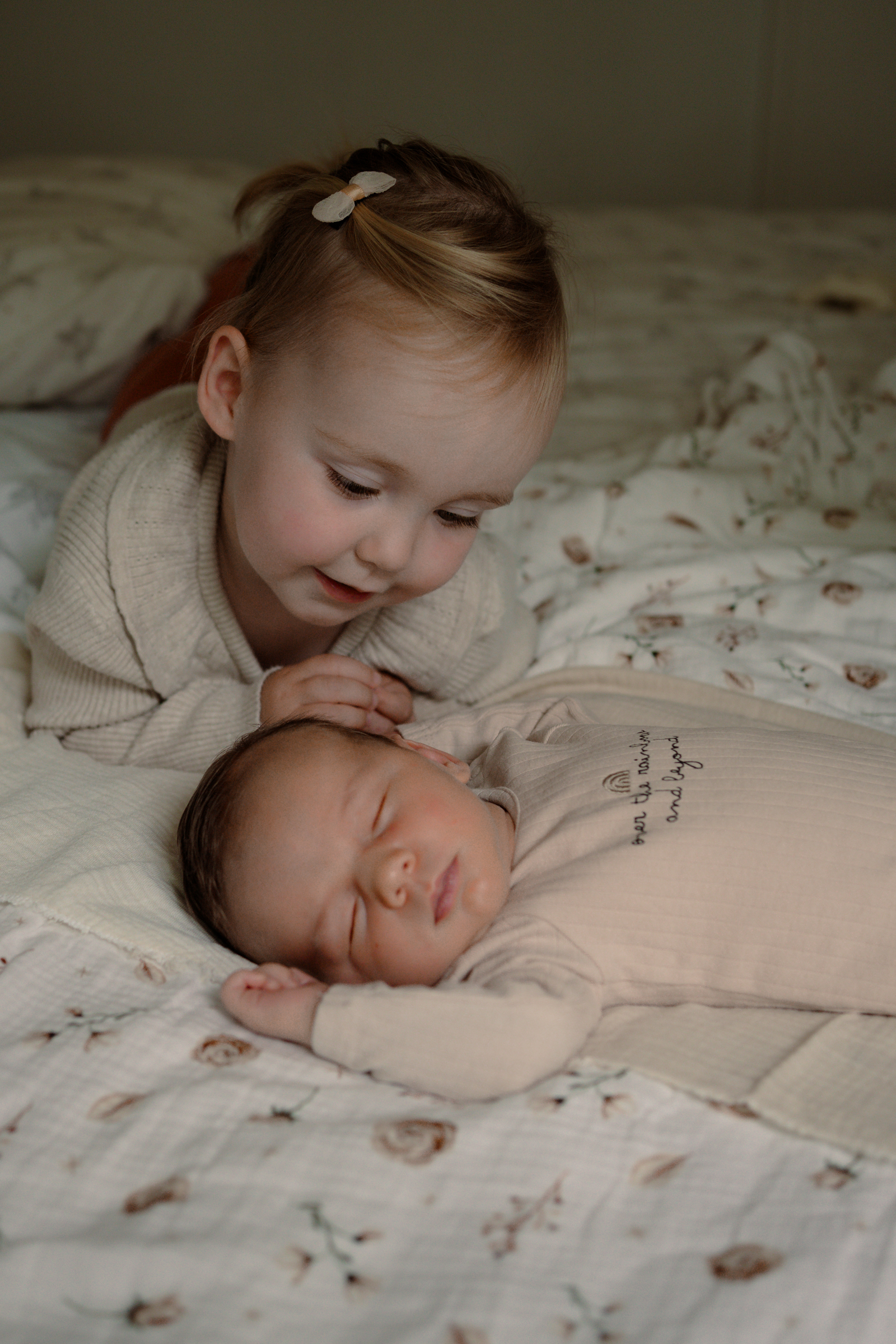 Zusje kijkt lief naar haar slapende baby broertje tijdens een newbornshoot aan huis in Apeldoorn