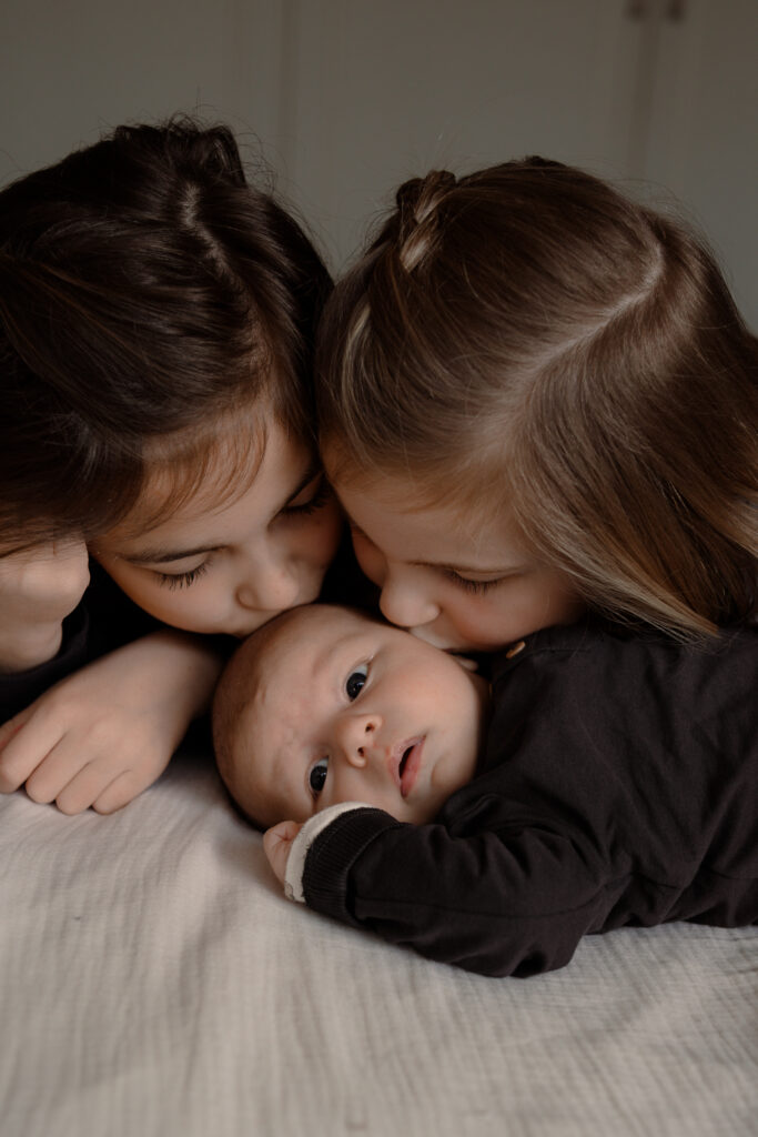 Grote zussen geven hun baby broertje een kusje tijdens een newbornshoot